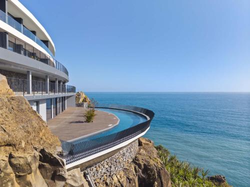 a building on a cliff next to the ocean at Oceanfront Elegance Madeira Retreat in Câmara de Lobos