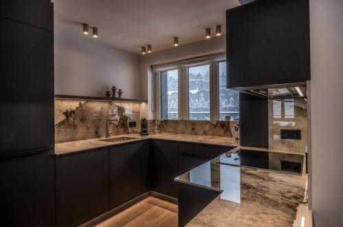 une cuisine avec des armoires noires et une grande fenêtre dans l'établissement JAMES TACC28 - exquisite apartment in the heart of Courchevel 1850, à Courchevel