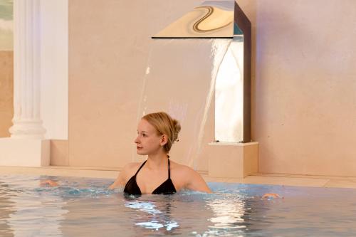 a woman in a swimming pool with a fountain at Rugard Thermal Strandhotel in Binz