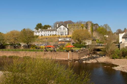 a bridge over a river with tables and umbrellas at The Castle Of Brecon Hotel, Brecon, Powys - The Coaching Inn Group in Brecon