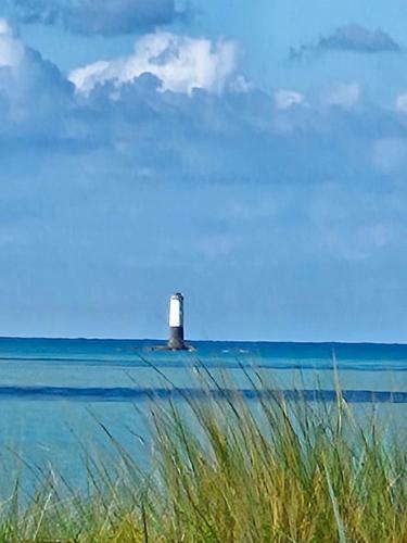 un phare sur l'eau avec une plage et de la pelouse dans l'établissement Esprit Mer, à Gouville-sur-Mer