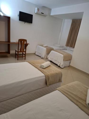 a room with three beds and a chair and a television at Brisas do Mar HOTEL & APART in Valença