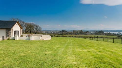 a large grassy field with a house and a fence at Bwthyn Gwenllyr in Llangadwaladr