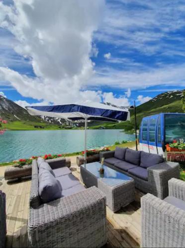 une terrasse avec des canapés et un parasol à côté d'un lac dans l'établissement Lo Terrachu, à Tignes