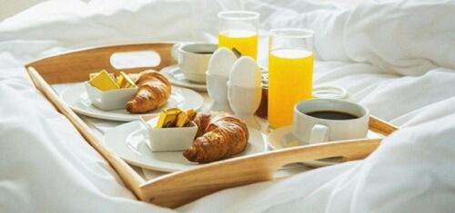 Una bandeja con alimentos y bebidas para el desayuno sobre una cama. en Illusion Suites, en Fira