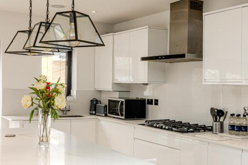 a white kitchen with a vase of flowers on a counter at Spacious 3BR Home with Garden & Parking, Ilford in Seven Kings