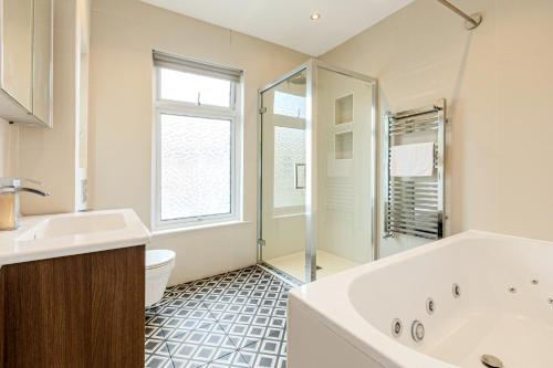 a bathroom with a tub and a toilet and a sink at Spacious 3BR Home with Garden & Parking, Ilford in Seven Kings