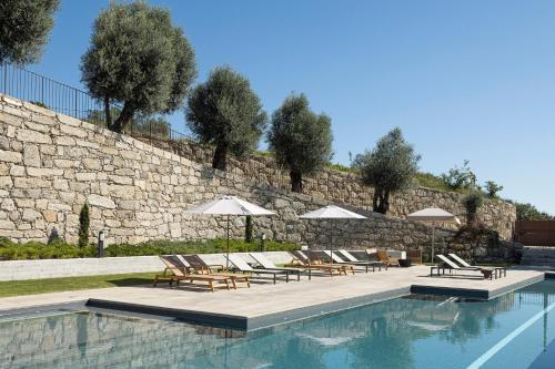a pool with chairs and umbrellas next to a stone wall at Quinta Leitão with 25m Pool & Gim by Sé Apartamentos in Vieira do Minho