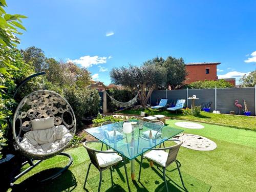 une terrasse avec une table en verre et des chaises sur une pelouse dans l'établissement Coco Lodge Home, maison cosy entre mer et nature !, à Vic-la-Gardiole