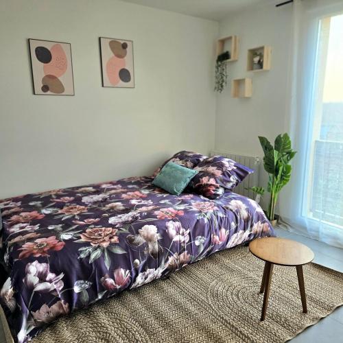 a bedroom with a bed with a floral bedspread and a table at Urban Zen - Freneuse in Freneuse