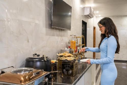 a woman standing in a kitchen preparing food at Lime Tree Hotel & One Bed Room Serviced Apartment - Noida Next to Sector 50 Metro with Party Venue in Noida