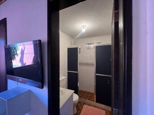 a bathroom with a toilet and a tv on the wall at Hospedagem do Iago in Cabo Frio