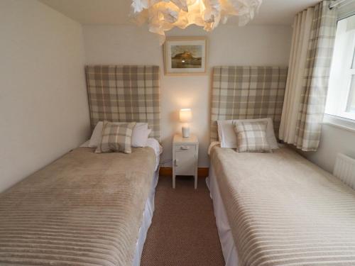 two beds in a small room with a lamp at Edendale in Longframlington