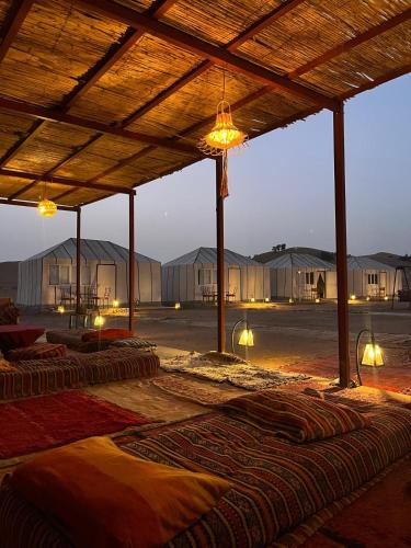 a group of mattresses under a wooden structure with lights at Bivouac Luna in Mhamid