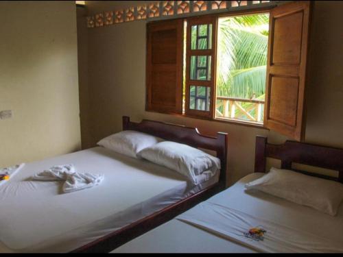 Dos camas en una habitación con ventana. en Posada Las Palmeras, en Bahía Solano