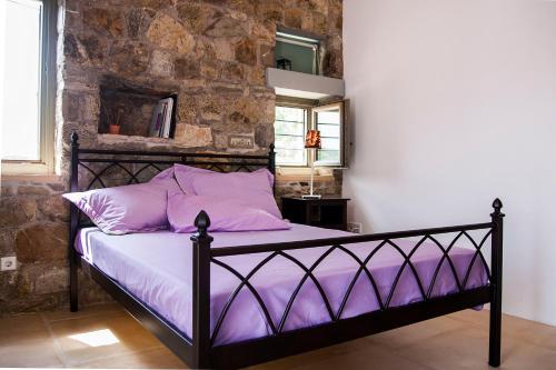 Una cama con sábanas moradas en una habitación con una pared de piedra. en Villa Penelope - Marathopoli, en Marathopolis