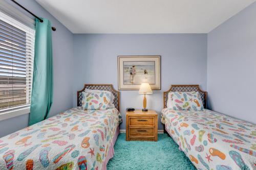 a bedroom with two beds and a table with a lamp at Ocean Dunes 306 by Carolina Beach Realty in Kure Beach