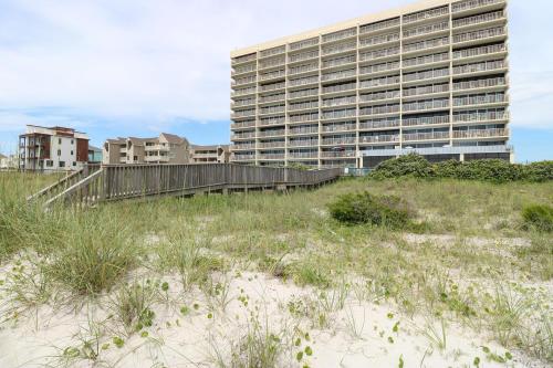 a building on the beach with a field of grass at Pelican Watch 706: Sea You Next Time by Carolina Beach Realty in Carolina Beach