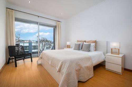 a white bedroom with a bed and a large window at Paim Apartments in Ponta Delgada