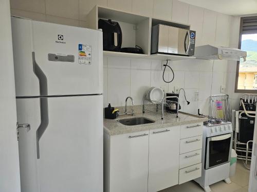 a white kitchen with a refrigerator and a sink at Loft Reserva do Sahy in Mangaratiba