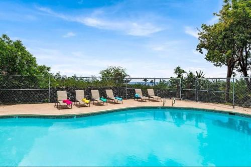 a large swimming pool with chairs and a fence at Kailani Kona-Ocean view, top floor Downtown w pool in Kailua-Kona