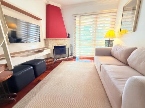 a living room with a white couch and a fireplace at Apartamentos Centrinho Capivari - Recanto Boticário in Campos do Jordão