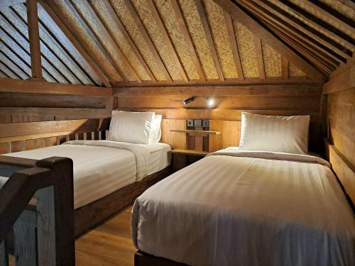 two beds in a room with wooden walls at Imalee - Cottage in Yogyakarta