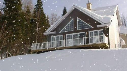 a house with a porch in the snow at Chalet Alpin in LʼAnse-Saint-Jean