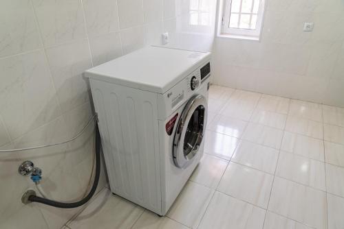 a white washing machine in a white tiled bathroom at Villa Musaler in Musalerr