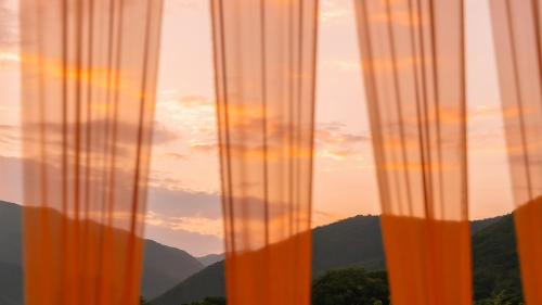 a view of the mountains through a window with curtains at Le Pavilion Pool Villa in Pohang
