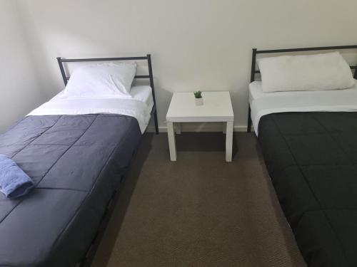 two beds in a room with a small table at Serenity Home 11 by Hiverooms in Pakenham