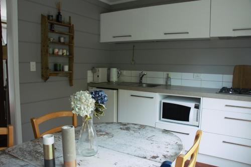 a kitchen with a table with a vase of flowers on it at Freshwaterfarm Cottages - Muriwai in Waimauku