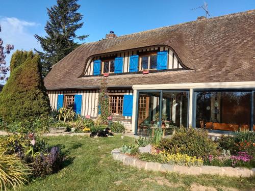 a house with blue windows and a cat laying in the yard at Chez Catherine - Chaumière Normande in Theuville-aux-Maillots
