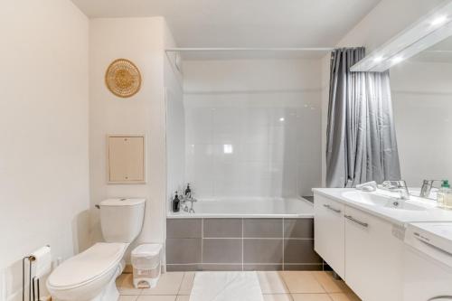 La salle de bains blanche est pourvue de toilettes, d'une baignoire et d'un lavabo. dans l'établissement Joli Studio haut standing à 100m du tram T3, à Villeurbanne