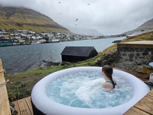 a woman in a bath tub next to a body of water at Sea View Suite in Klaksvík