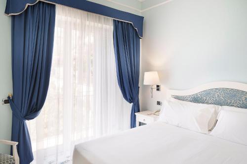 a bedroom with a bed and a window with blue curtains at Hotel Raito Wellness & SPA in Vietri sul Mare