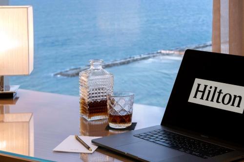 a laptop computer sitting on a desk with a bottle and a glass at The Vista At Hilton Tel Aviv in Tel Aviv