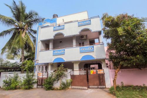 a tall white building with blue windows and a palm tree at Hotel O Vivekam Home Stay in Coimbatore