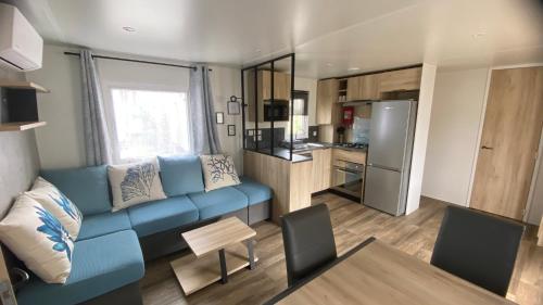 un salon avec un canapé bleu et une cuisine dans l'établissement MH 541 Spacieux 40m2 avec 2 chambres 1 salle de bain dans Camping 4 étoiles, à Saint-Julien-en-Born