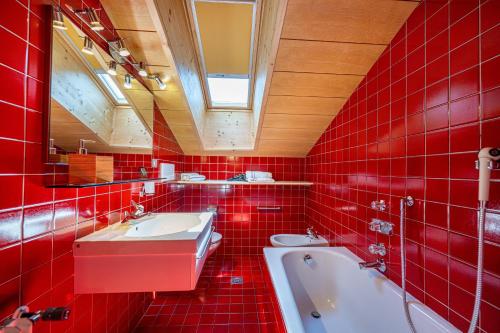 a red tiled bathroom with a sink and a tub at Panorama Apartments Walter in Ortisei