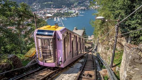 a purple train on the tracks next to a lake at B&B Villa Mirandola in Brunate