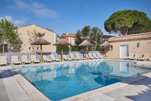 a large swimming pool with chairs and umbrellas at Résidence Odalys Le Mas des Flamants in Aigues-Mortes