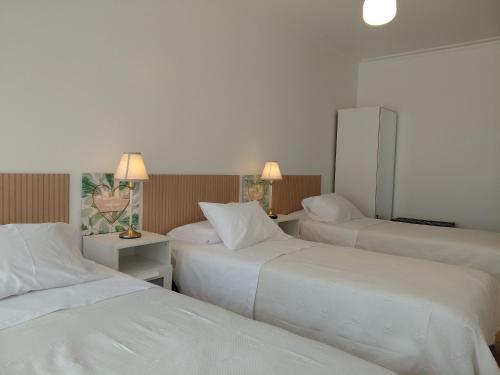 ein Hotelzimmer mit drei Betten mit weißen Laken in der Unterkunft Vila Morena in Grândola