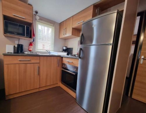 une cuisine avec un réfrigérateur en acier inoxydable et des armoires en bois dans l'établissement LOCATION MOBIL HOME 40m carré de 2 à 8 personnes en bords de mer, à Saint-Brévin-lʼOcéan