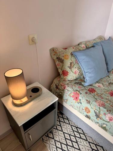 a bed with a night stand with a lamp on it at Rokiskis- jaukus butas su balkonu in Rokiškis
