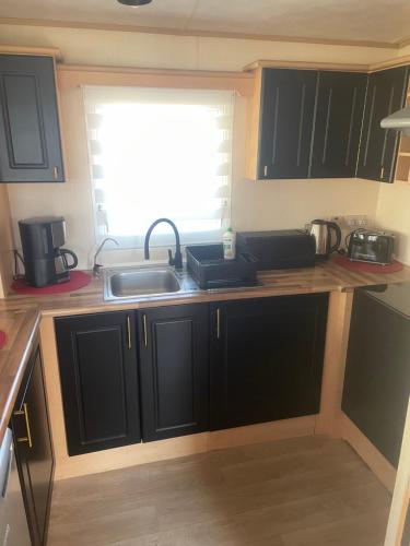 a kitchen with black cabinets and a sink and a window at MIĘDZY NAMI domki nad jeziorem in Kołczewo