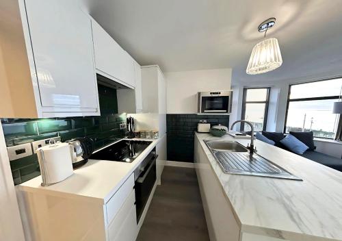 a kitchen with white cabinets and a sink and a couch at Granada Apartments Berkeley in Blackpool