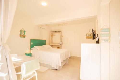 a white bedroom with a bed and a table at Casa d'Aroeira Residencial Boutique - Centro de Juqueí - 2 quadras do mar - Serviço de Praia - Roupa de Cama 600 fios algodão Egípcio - Toalhas Banho e Praia - Tudo Novo - Estacionamento Interno - Cozinha - Consulte unidades com Ofurô Hidro e Cromoterapia in Juquei