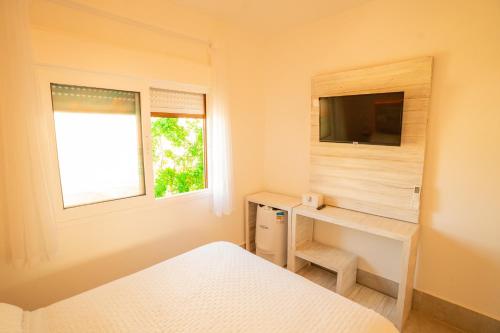 a bedroom with a bed and a desk with a television at Casa d'Aroeira Residencial Boutique - Centro de Juqueí - 2 quadras do mar - Serviço de Praia - Roupa de Cama 600 fios algodão Egípcio - Toalhas Banho e Praia - Tudo Novo - Estacionamento Interno - Cozinha - Consulte unidades com Ofurô Hidro e Cromoterapia in Juquei