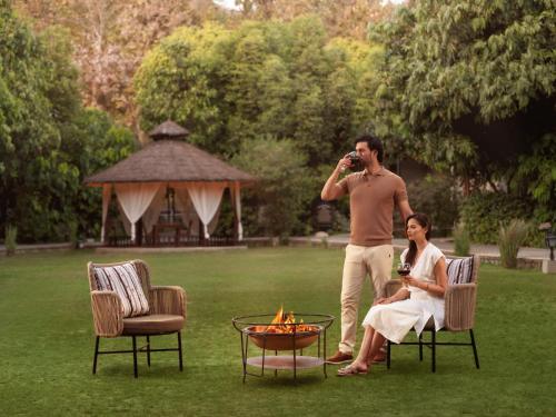 a man taking a picture of a woman sitting next to a fire at Aahana Resort - Jim Corbett in Rāmnagar